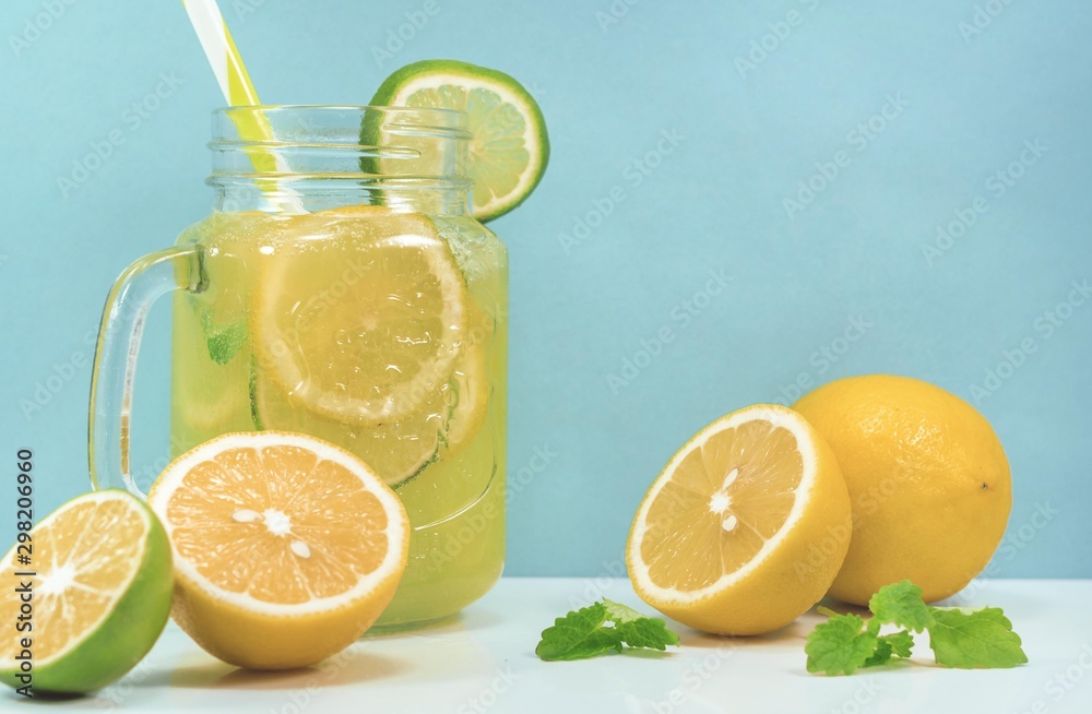 Lemonade drink of soda water, citrus and mint on the light blue background. Cocktail glass with handle and straw, sliced lemon and lime, front view Lemonade drink of soda water, citrus and mint on the light blue background. Cocktail glass with handle and straw, sliced lemon and lime, front view