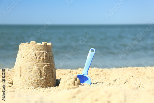 Fototapeta Naklejka Na Ścianę i Meble -  Beautiful view of beach with sand figure and shovel near sea. Space for text