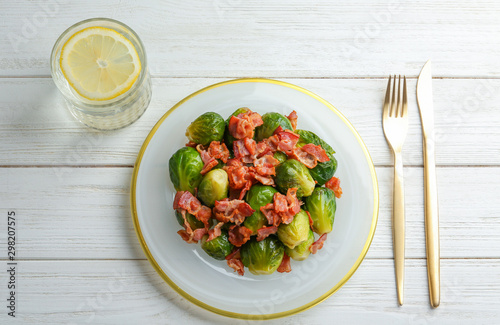 Flat lay composition of tasty roasted Brussels sprouts with bacon on white wooden table