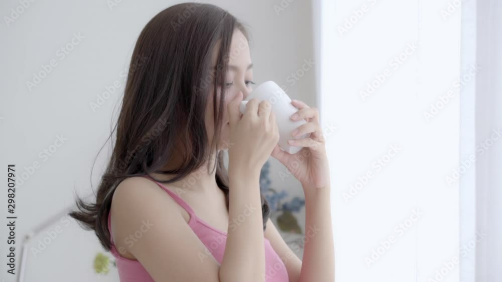Beautiful portrait young asian woman smile and drink a cup of coffee with relax in the morning at window, girl happy with leisure breakfast is beverage for fresh, lifestyle concept, slow motion. Beautiful portrait young asian woman smile and drink a cup of coffee with relax in the morning at window, girl happy with leisure breakfast is beverage for fresh, lifestyle concept, slow motion.