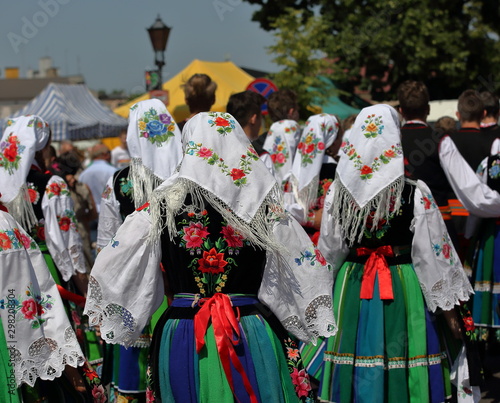 Group of girls walk on their back, wear traditional colorful folk costumes from Lowicz region, Poland