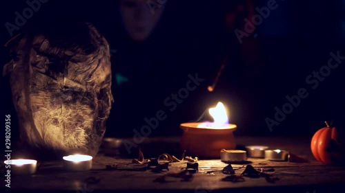 Horror and scary witch in white mask making spell and curse in the Halloween night in front of a mummy head.