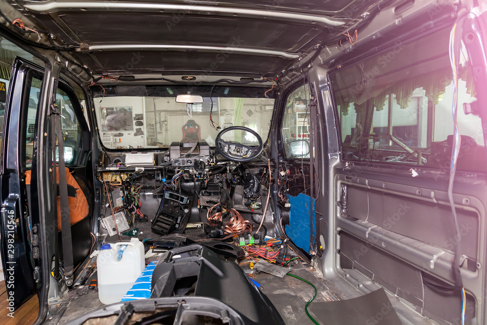 Car interior in the back of a van with a disassembled dashboard and view on steering wheel during preparation in a vehicle repair workshop. Auto service industry