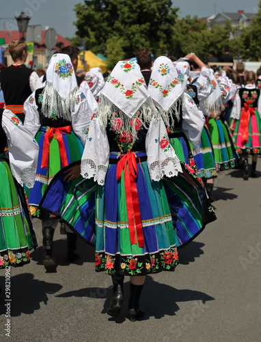 Local Polish girls in traditional folk costumes from lowicz region walk in street while celebrate Corpus Christi holiday, on their back