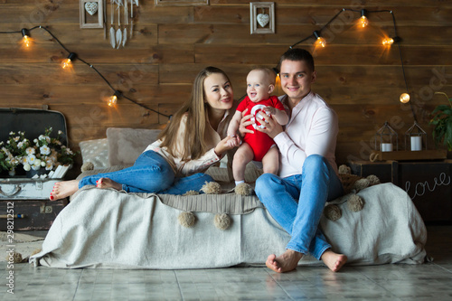 Parents and their child sitting on bed. Mom, dad and baby. Portrait of young family. Happy family life. Man was born.