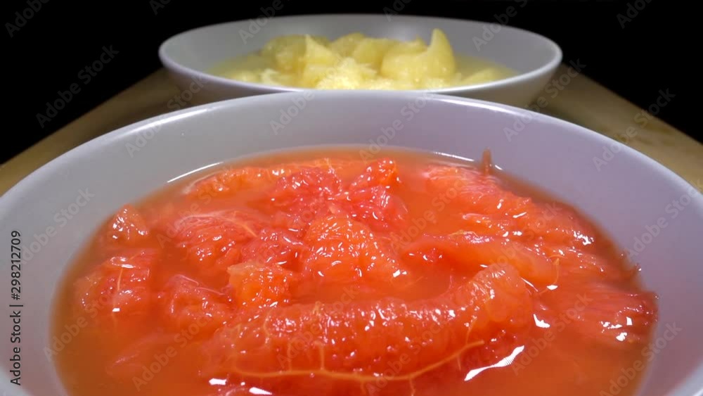 Slow motion close POV reverse dolly shot of a bowl of normal sliced grapefruit at the rear, with a bowl of ruby red grapefruit slices at the front. Slow motion close POV reverse dolly shot of a bowl of normal sliced grapefruit at the rear, with a bowl of ruby red grapefruit slices at the front.
