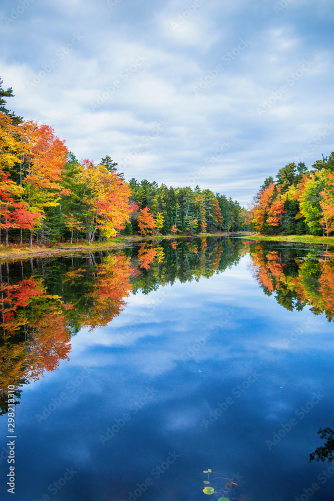 Fall foliage colors reflected in still lake water on a beautiful autumn day in New England