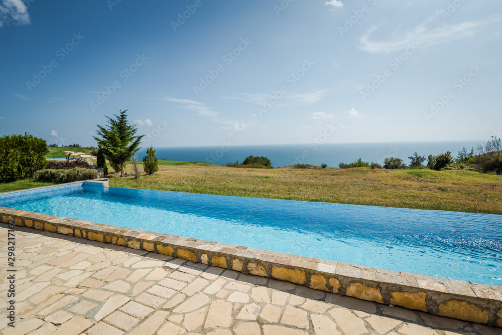Outdoor swimming pool. Holiday villa exterior with a great scenery - green grass garden and an ocean 