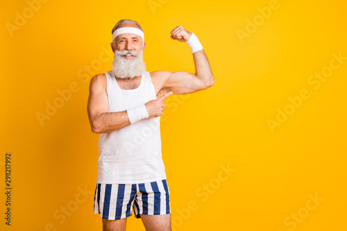Photo of cheerful positive toothy beaming man pointing at his biceps to show results of his work isolated vivid yellow color backgroun