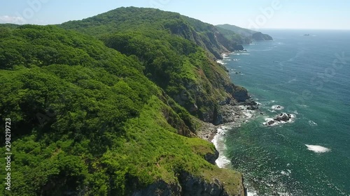 Flight forward coastline green forest blue sea. Sunny weather. Meditation beautiful Russia Far East. Calm cinematic drone photo