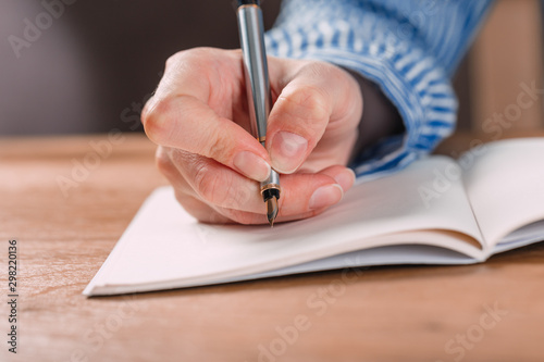 Beautiful Female hands write pen in a notebook of tasks and goals to work on a wooden table