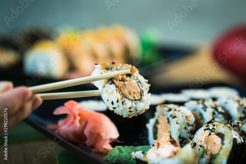 Eating roll sushi in japanese restaurant, hand with chopsticks closeup.. California Sushi roll set with salmon, vegetables.