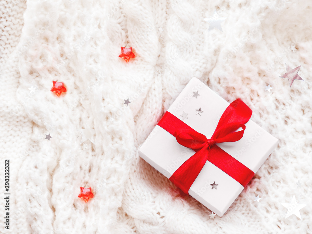 Present in white wrapping paper on white knitted backdrop. Holiday gift with red ribbon and bow. Present in white wrapping paper on white knitted backdrop. Holiday gift with red ribbon and bow.