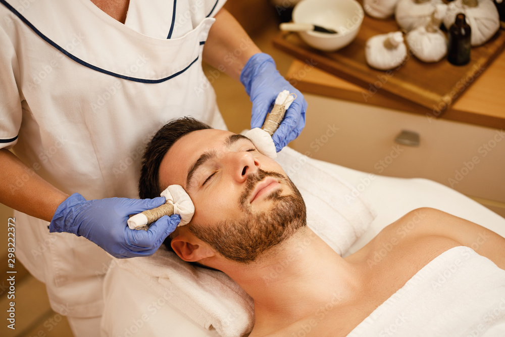 Young man receiving head massage with herbal balls at the spa. Young man receiving head massage with herbal balls at the spa.