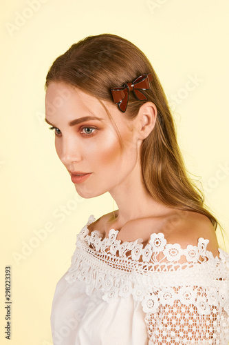 Medium close-up shot of a young stylish European girl with a cambered hair clip in her long straight hair. The hairpin is made of burgundy glazy material in the form of a bow-knot with a black stripe.