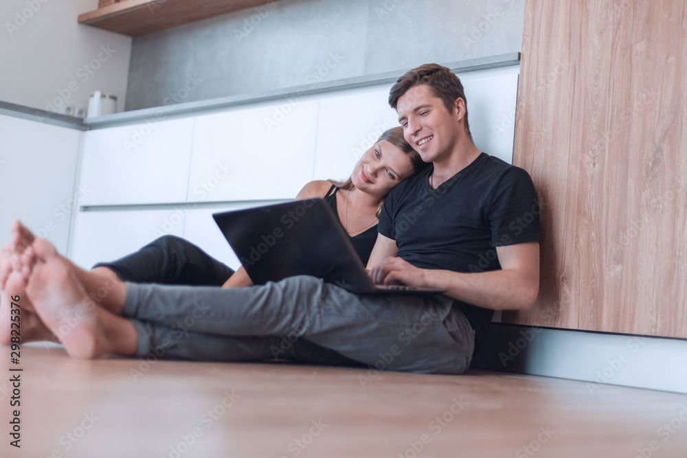 young couple uses a laptop sitting on the floor of a new apartment