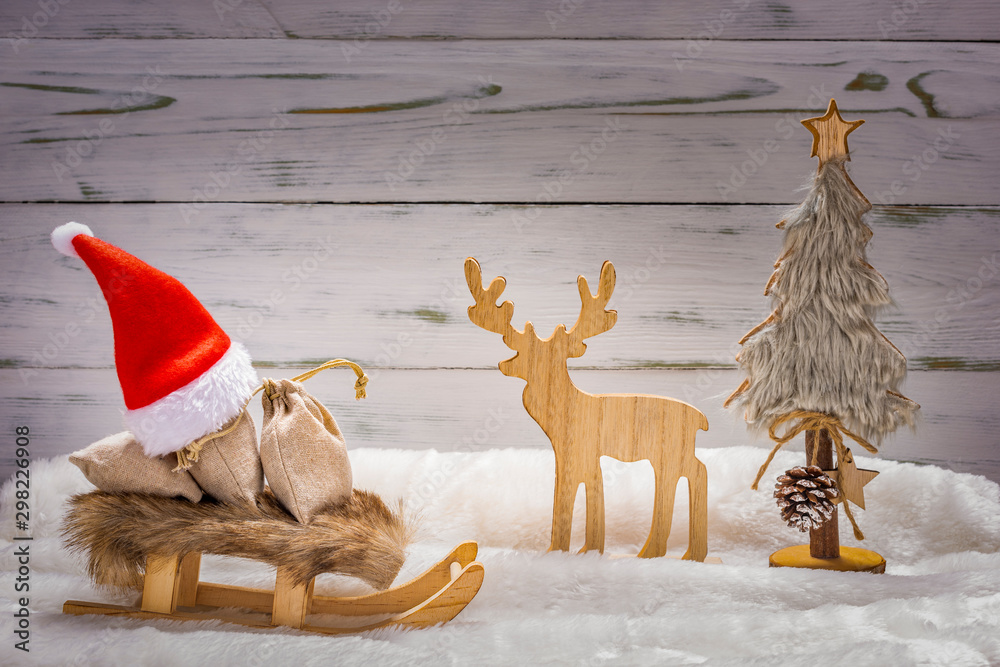 Weihnachtsmütze mit Schlitten und Geschenke, ein Rentier und Weihnachtsbaum im Schnee vor einem Holz Hintergrund