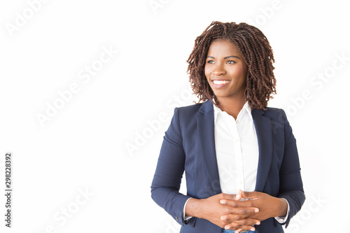 Happy female business leader posing with clasped hands. Young black business woman standing isolated over white background, looking at copy space away, smiling. Advertising concept