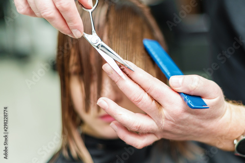 Hands of hairdresser is cuting hair close up. Hair stylist cuts hair of woman close up.