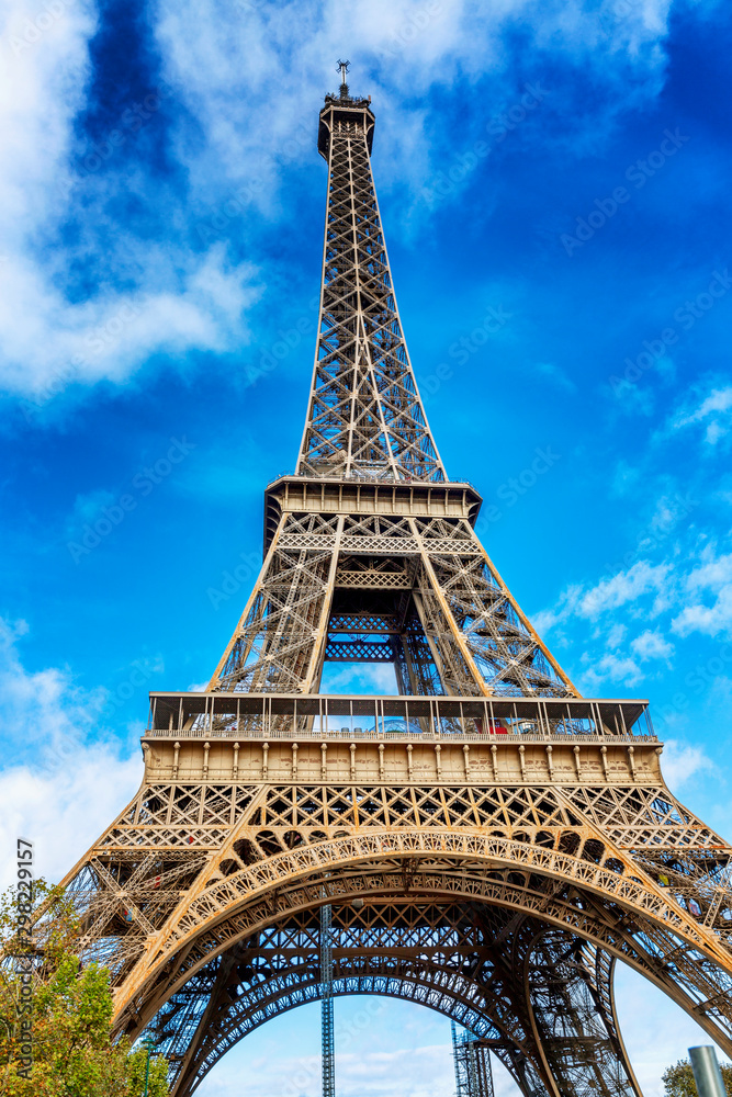 Eiffel Tower in the green of the trees against the blue sky on a bright sunny day. Vertical.