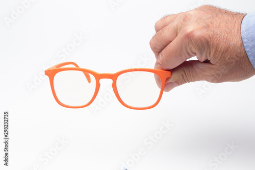 Gafas y lentes de colores y montura de plástico, de diseño, sobre fondo blanco y en la mano de una persona adulta; gafas con cristales graduados para mejorar la visión de las personas