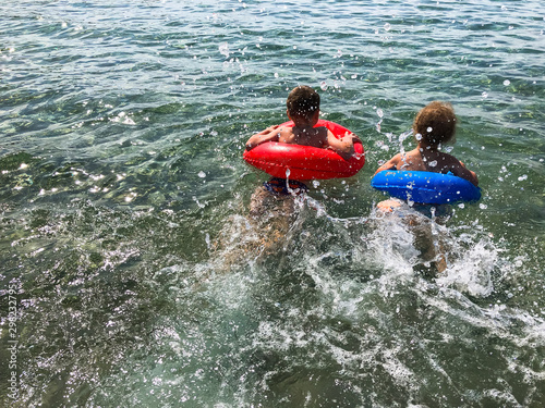 Two kids are swimming with rubber circles. Children's beach vacation at sea