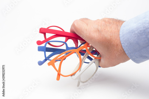 Gafas y lentes de colores y montura de plástico, de diseño, sobre fondo blanco y en la mano de una persona adulta; gafas con cristales graduados para mejorar la visión de las personas