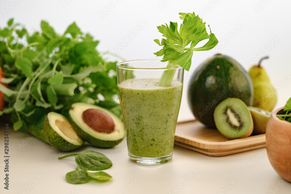 Green smoothie with a stalk of celery in a glass cup. On the table is an avocado. Green smoothie with a stalk of celery in a glass cup. On the table is an avocado.