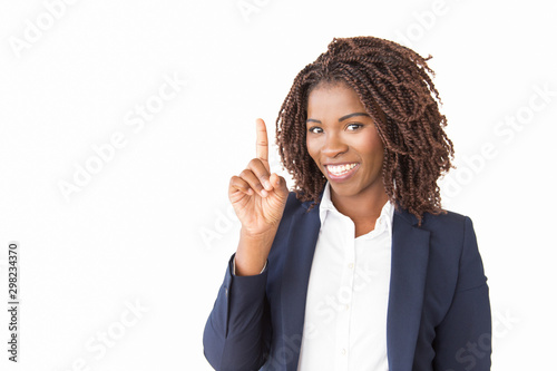 Happy young businesswoman pointing finger up at copy space. African American business woman standing isolated over white background, looking at camera, smiling. Advertising concept photo