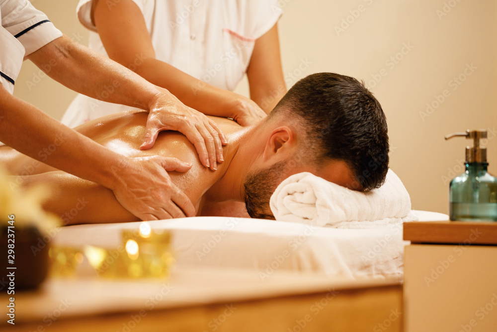 Fototapeta premium Unrecognizable man receiving back massage by two therapists at the spa.