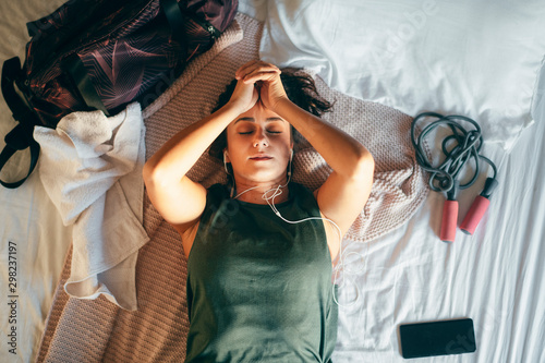 Young woman after training lying on bed and listening music