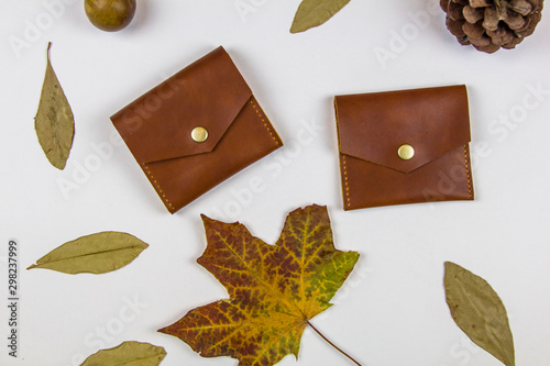 leather wallets and dry autumn leaves on a white background, top view