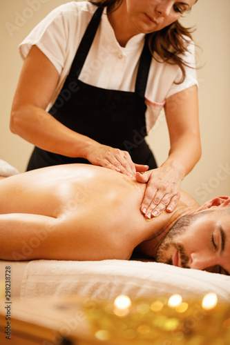 Young man enjoying in relaxing back massage with honey at the spa.