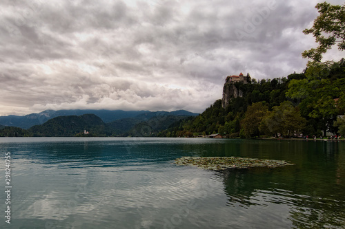 Stunning nature landscape of Bled Lake. Ancient Castle on the top of the rock. Famous island with church at the background. Stormy clouds reflected at the turquoise water. Bled, Slovenia