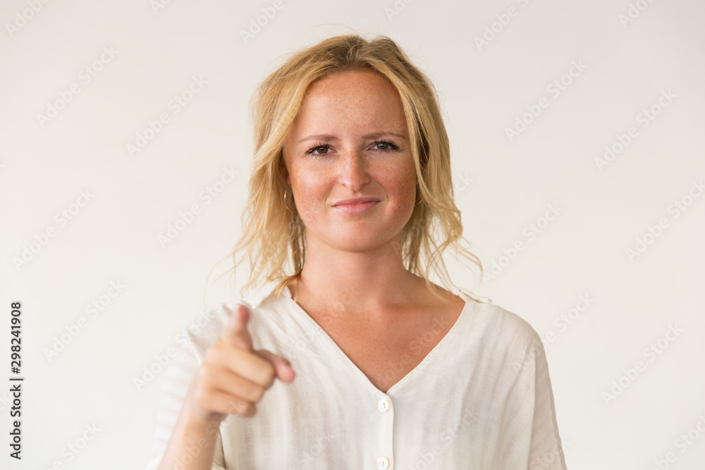 Smiling woman pointing at camera. Portrait of beautiful young blonde woman pointing with finger and looking at camera. Gesture concept Smiling woman pointing at camera. Portrait of beautiful young blonde woman pointing with finger and looking at camera. Gesture concept