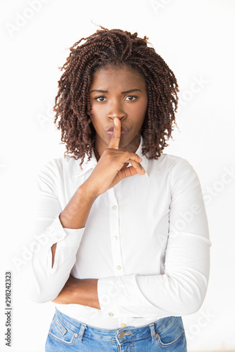 Excited silent young woman making shh gesture. Young African American businesswoman posing isolated over studio background, applying index finger at mouth. Secret concept
