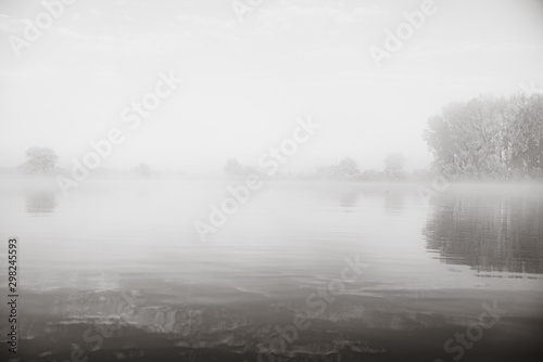 Autumn calm morning on meadow with river. Beautiful sunrise over field with sunlight and mist.Black and white photo