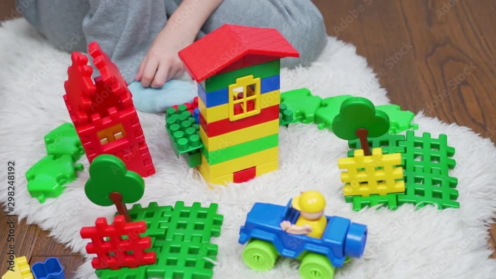 Happy child fun playing with colored blocks designer, he collected a beautiful house, a clearing at the house with trees and a car with a driver. Children and toys. Camera slide Happy child fun playing with colored blocks designer, he collected a beautiful house, a clearing at the house with trees and a car with a driver. Children and toys. Camera slide