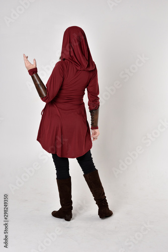 full length portrait of a girl wearing fantasy long red hooded tunic. standing pose with back to the camera.