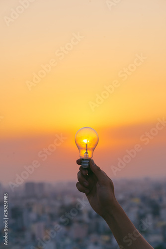 Hand hold a light bulb on sunset background for saving energy and creative concept.