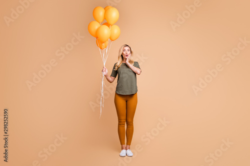 Full body photo of amazing charming blond lady emotional surprise holding bright orange balloons came birthday party wear green t-shirt trousers isolated beige color background