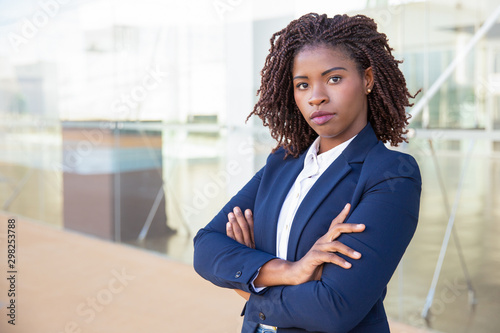 Serious successful professional posing near office building. Young African American business woman with arms crossed standing outside, looking at camera. Confident businesswoman concept
