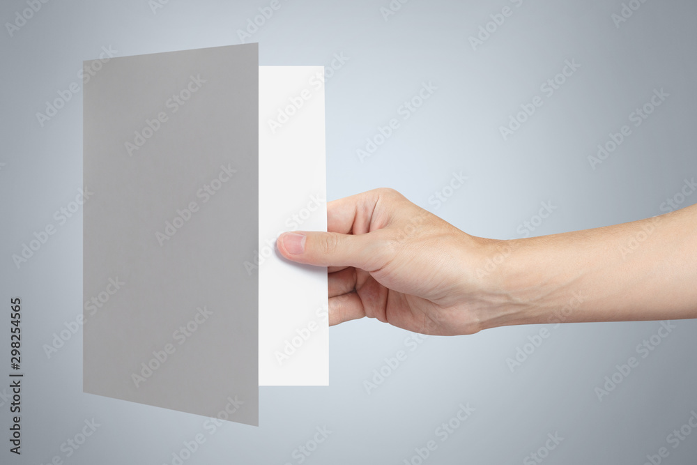 Hand holding a sheet of white paper, folded in half on gray background Hand holding a sheet of white paper, folded in half on gray background