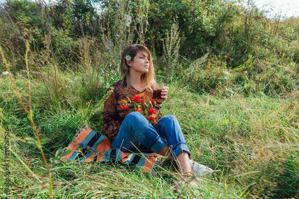 Beautiful woman with camomile flower in hair sitting on the grass and drinking tea outdoors Beautiful woman with camomile flower in hair sitting on the grass and drinking tea outdoors