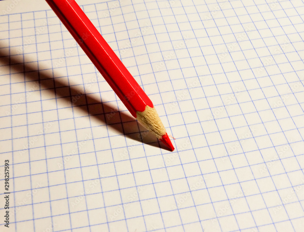 A red pencil on a checkered notebook sheet. A red pencil on a checkered notebook sheet.