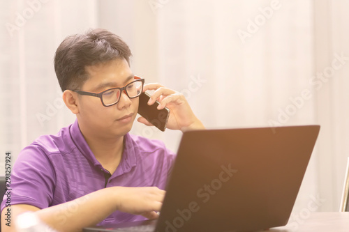 The office worker in a purple shirt is working on a laptop and talking on the phone. Asian employees work overtime in the office.