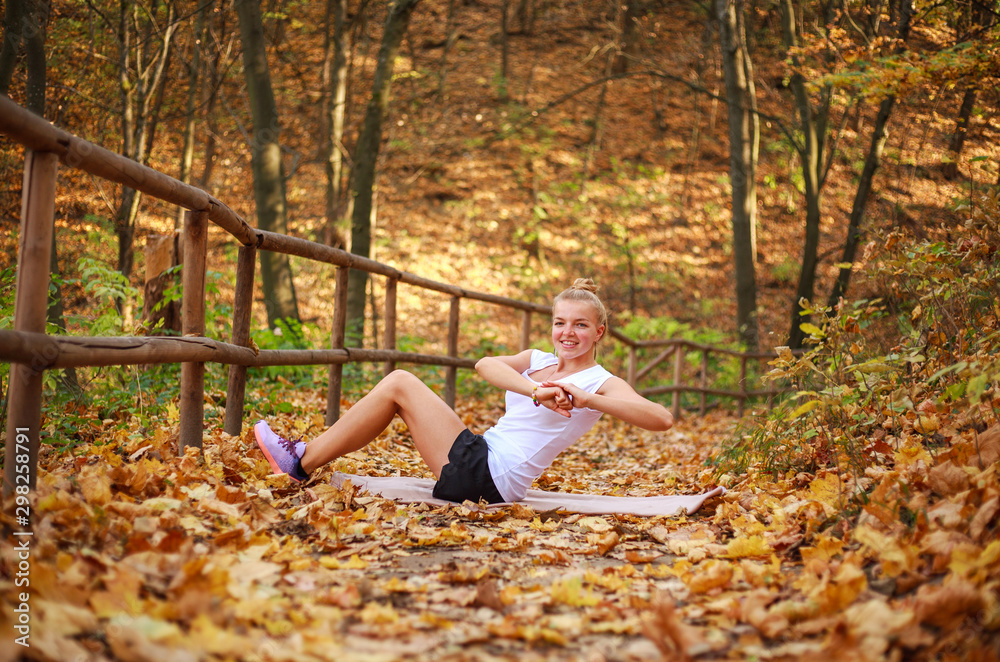 Joyful sports girl doing fitness exercises, warming up in forest park in autumn, healthy lifestyle, outdoor activities