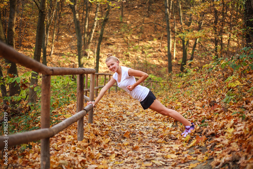 Joyful sports girl doing fitness exercises, warming up in forest park in autumn, healthy lifestyle, outdoor activities