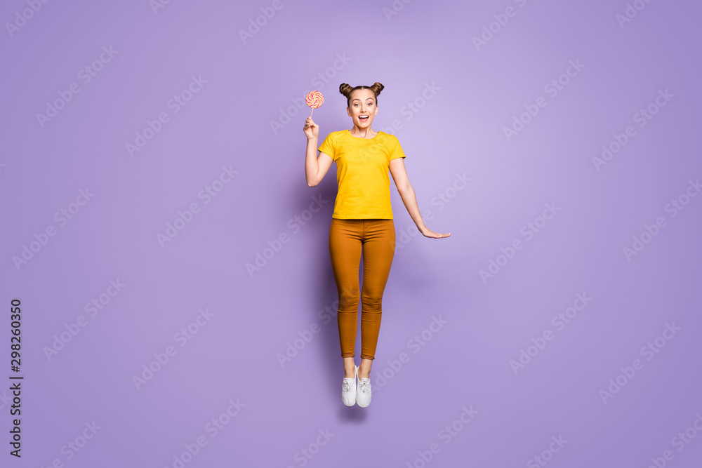 Full length body size photo of cheerful positive cute nice charming girlfriend jumping with excited feelings after tasting her candy wearing brown trousers pants footwear isolated over violet pastel Full length body size photo of cheerful positive cute nice charming girlfriend jumping with excited feelings after tasting her candy wearing brown trousers pants footwear isolated over violet pastel