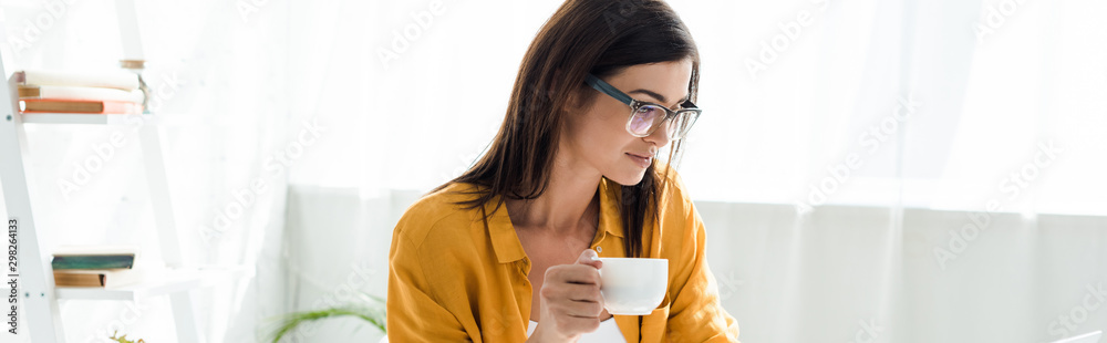 beautiful female freelancer in eyeglasses holding cup of coffee in home office - obrazy, fototapety, plakaty 